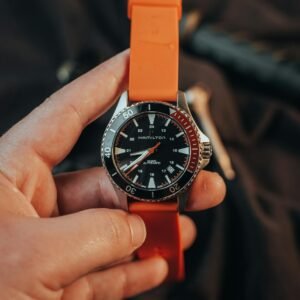 A modern wristwatch with an orange strap held by an adult's hand, showcasing stylish design.