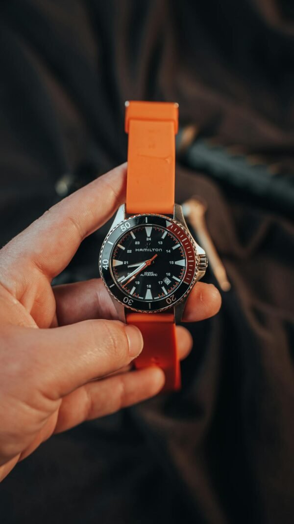 A modern wristwatch with an orange strap held by an adult's hand, showcasing stylish design.