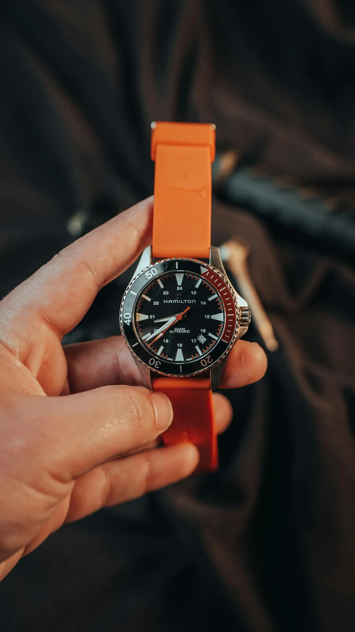 A modern wristwatch with an orange strap held by an adult's hand, showcasing stylish design.