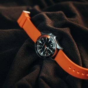 Close-up of a sleek watch with vivid orange strap, set on dark fabric for fashion appeal.