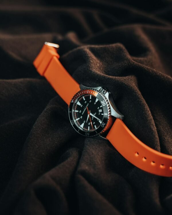 Close-up of a sleek watch with vivid orange strap, set on dark fabric for fashion appeal.