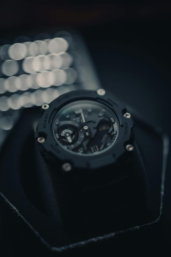 High-contrast close-up of a black wristwatch featuring intricate details against a blurred bokeh background.